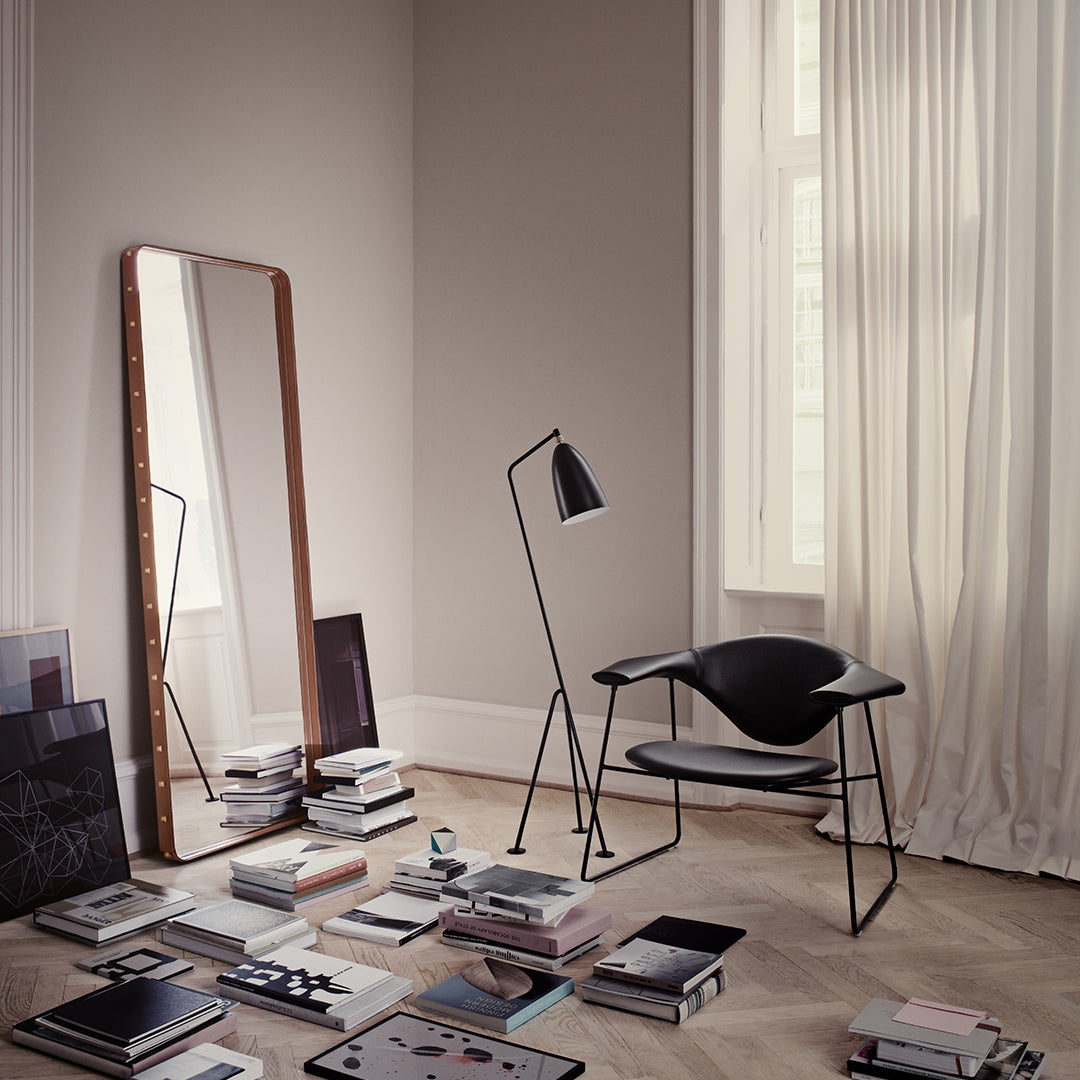Elegant black chair and lamp amidst neutral walls, light wood floor, and stacks of monochrome books in a serene setting.