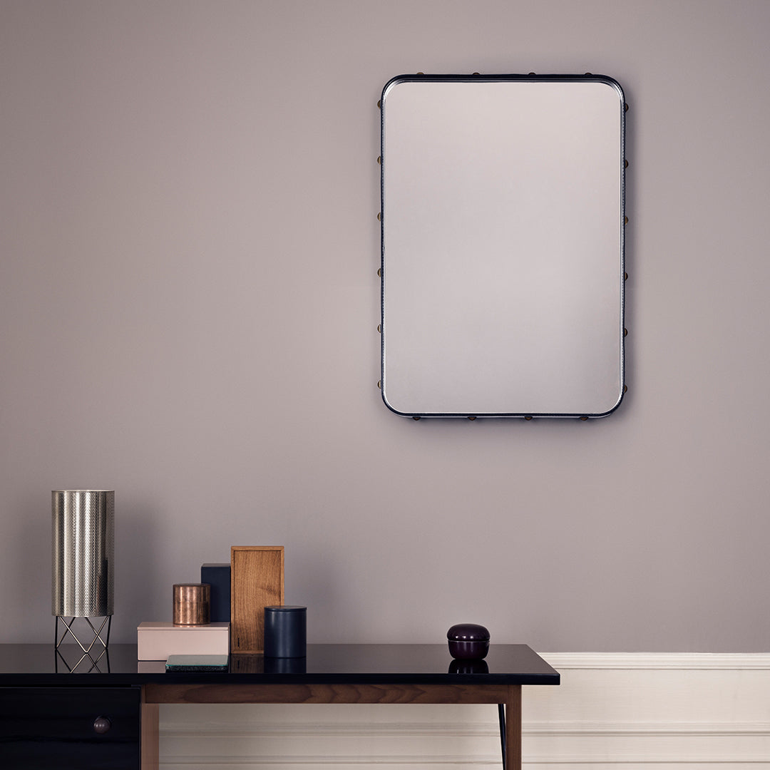 Rectangular mirror with a black frame against a soft gray wall; elegant vases in muted colors on a wooden table.