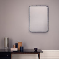 Rectangular mirror with a black frame against a soft gray wall; elegant vases in muted colors on a wooden table.