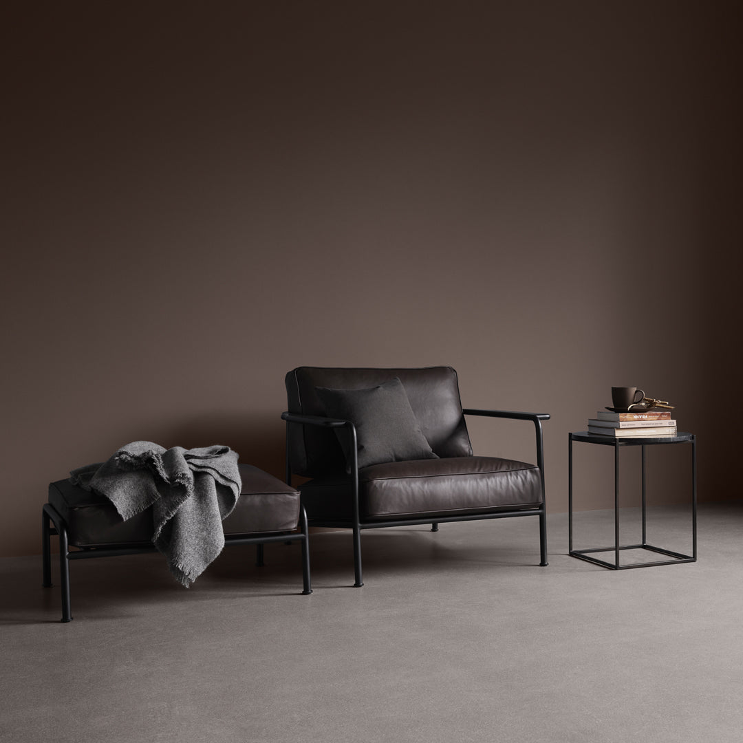 Stylish black leather chair and ottoman on a neutral gray floor with a minimalist black side table.