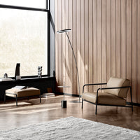 "Modern beige chair and stool with sleek black metal accents in a light-filled wood-paneled interior."