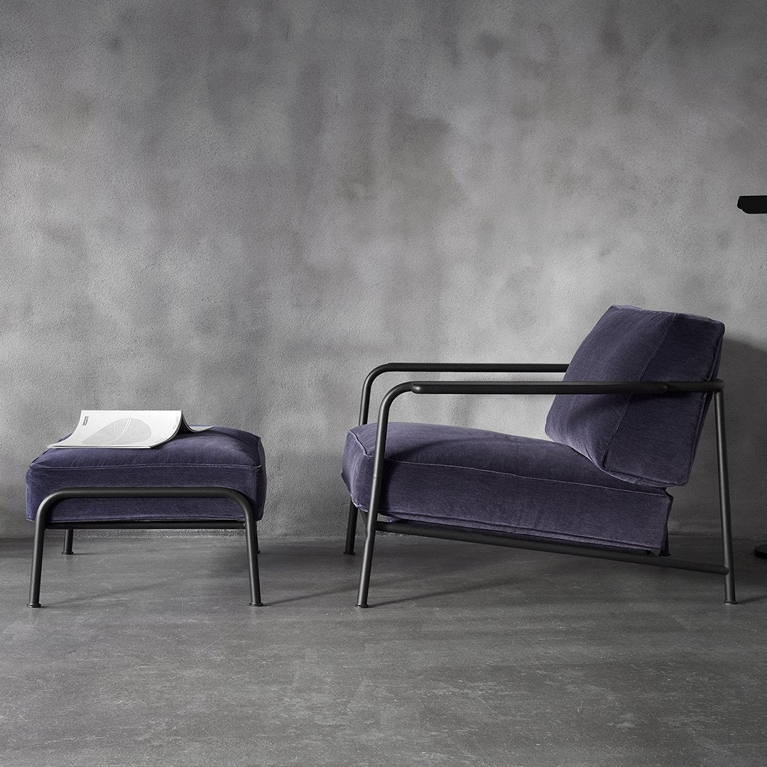 Navy blue velvet lounge chair and ottoman with sleek black metal frames against a minimalist gray backdrop.