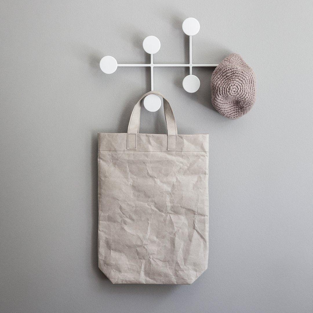 Beige crumpled tote bag hanging against a light gray wall, accompanied by a textured light brown hat.