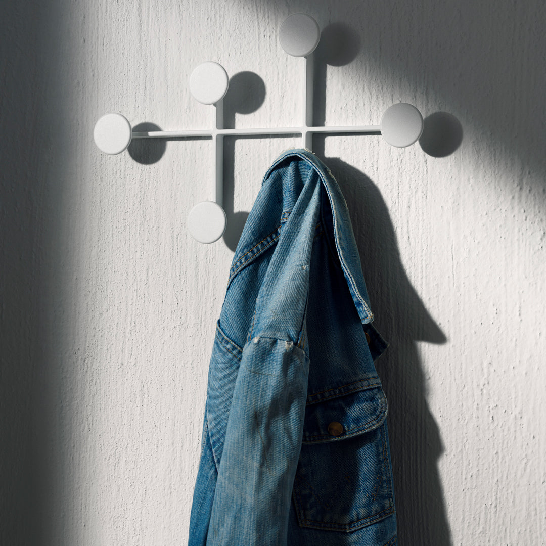 Modern white wall hook with circular accents, featuring a textured denim jacket hanging against a textured white background.
