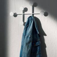 Modern white wall hook with circular accents, featuring a textured denim jacket hanging against a textured white background.