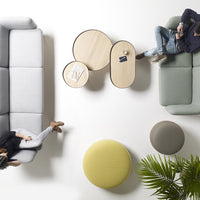 Modern living room setup featuring gray and light green sofas, round light wood tables, and colorful poufs in yellow and gray.