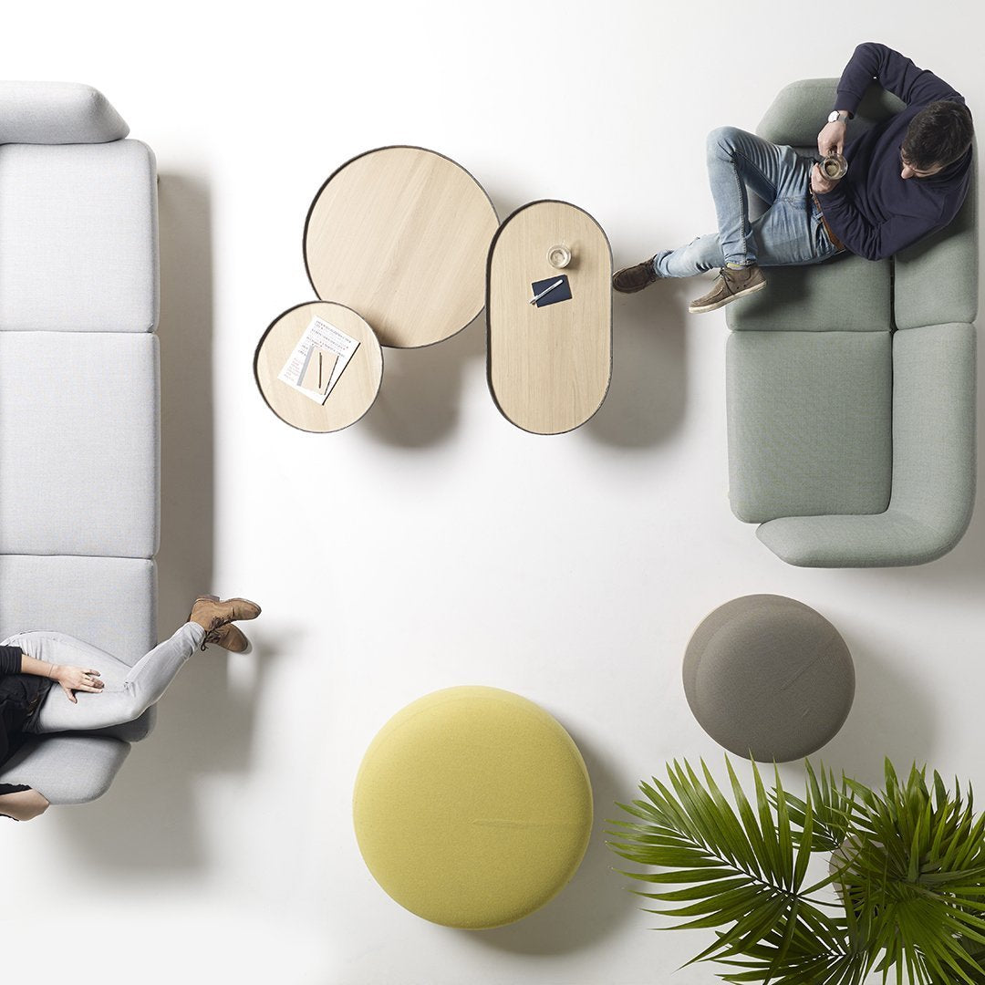 Minimalist living room with gray and green sofas, circular wooden tables, and colorful poufs in yellow and beige tones.