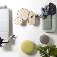 Minimalist living room with gray and green sofas, circular wooden tables, and colorful poufs in yellow and beige tones.
