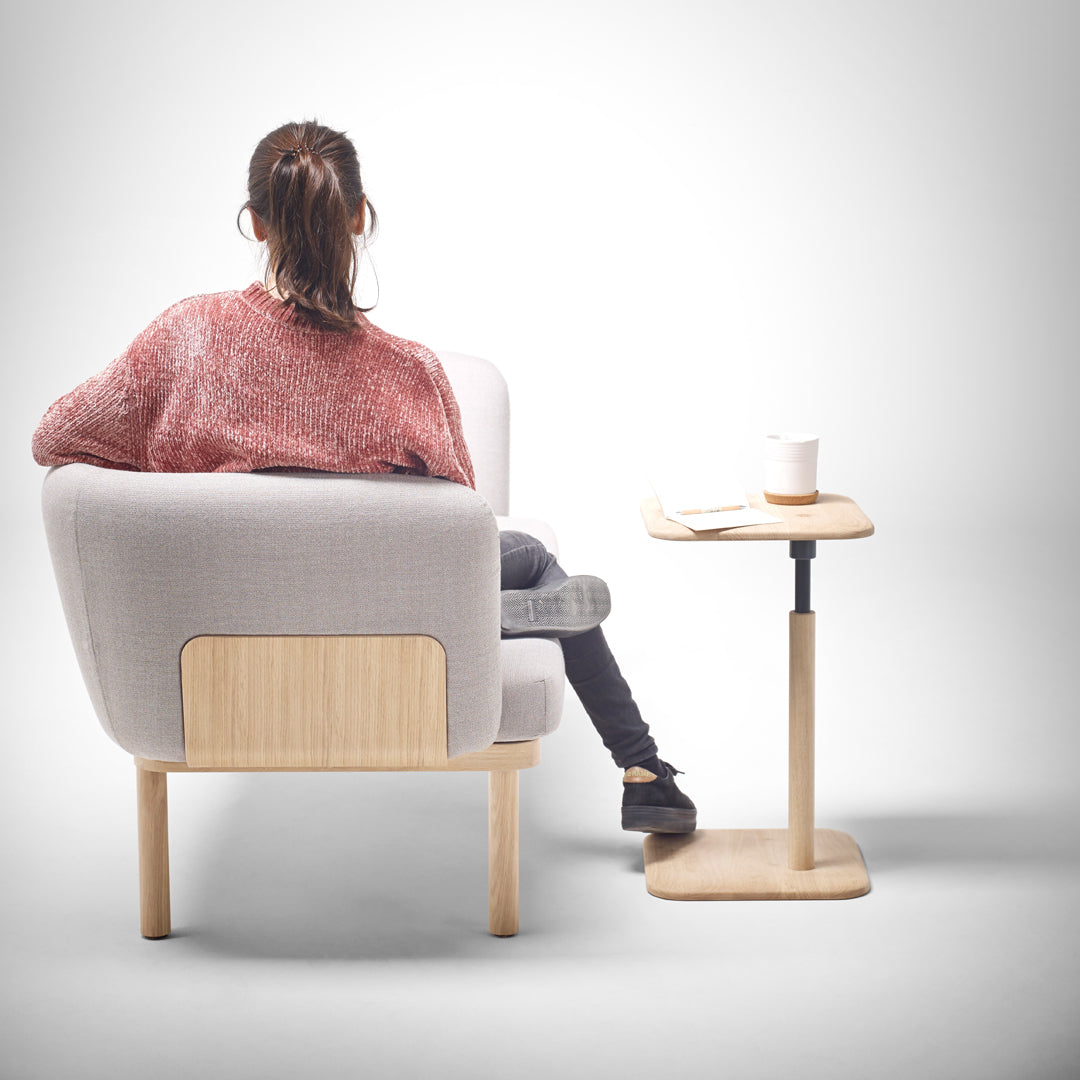 Cozy gray armchair with wooden accents and a textured pink sweater, paired with a minimalist light wood side table.