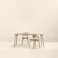 Light wood dining table and two chairs in beige and coral, with simple, modern design against a soft cream background.