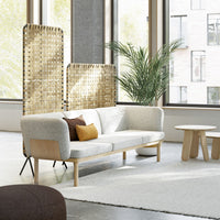 Modern light gray sofa with wooden accents, featuring textured beige cushions and a natural woven screen backdrop.
