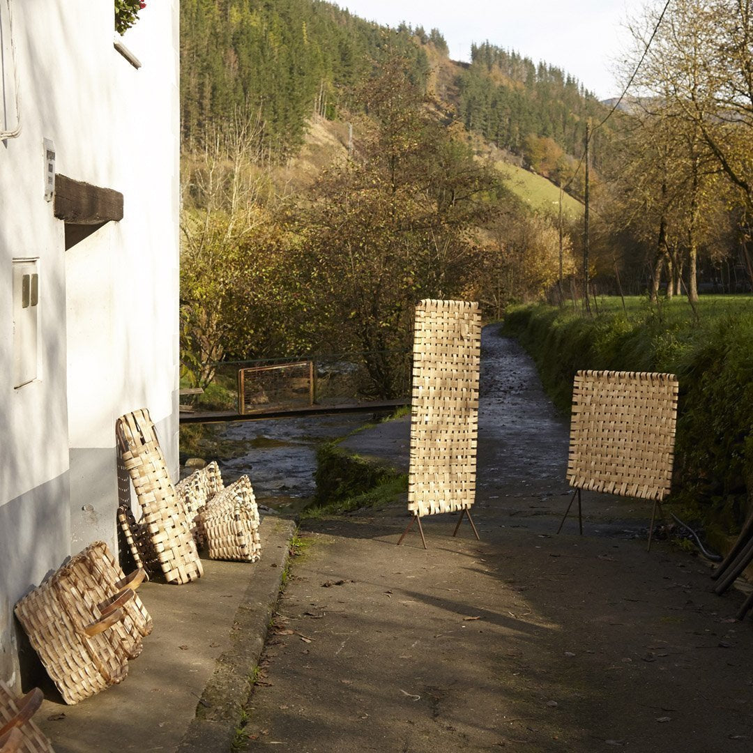 Natural woven textures in light beige and brown tones against a serene outdoor backdrop of greenery and water.
