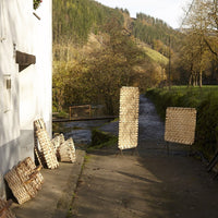 Natural woven textures in light beige and brown tones against a serene outdoor backdrop of greenery and water.