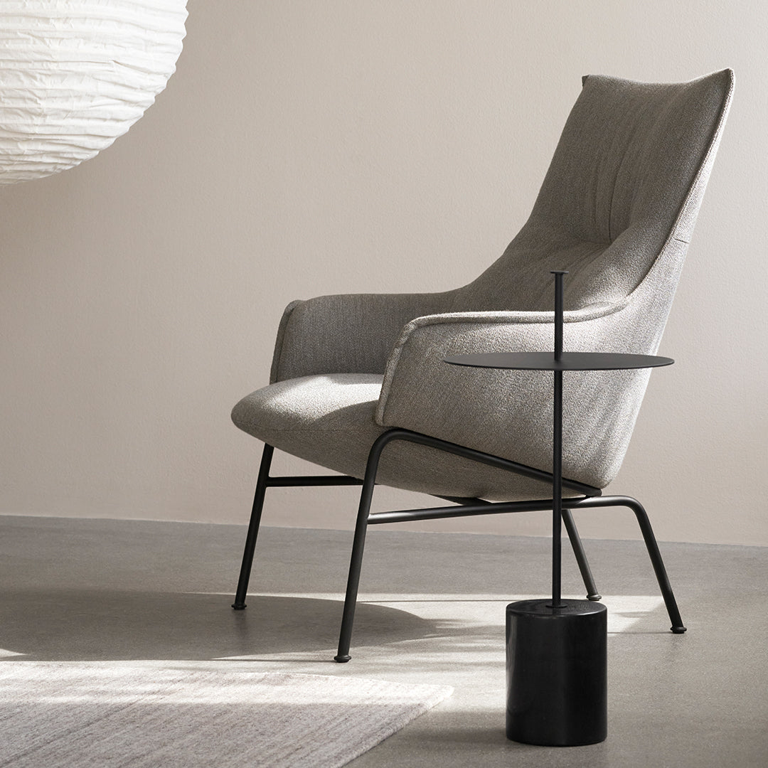 Gray upholstered chair with sleek black metal legs, paired with a minimalist round side table in a modern setting.