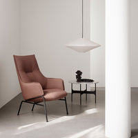 Elegant blush pink armchair with a minimalist black frame, paired with a sleek white pendant light and modern decor.