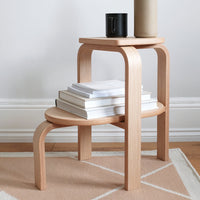 Light wood finish side table with smooth curves and a minimalist design, featuring a beige geometric rug beneath.