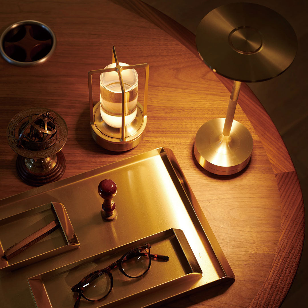 Gold-toned decor on wooden table featuring a metallic lamp, candle holder, and trays in rich, warm hues.