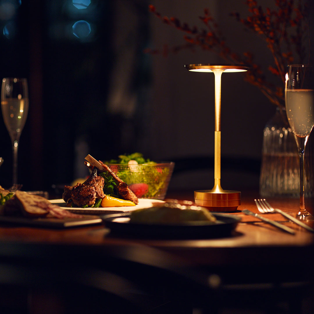 Gold table lamp with a sleek design, glowing softly against a dark backdrop, surrounded by rich, inviting food colors.
