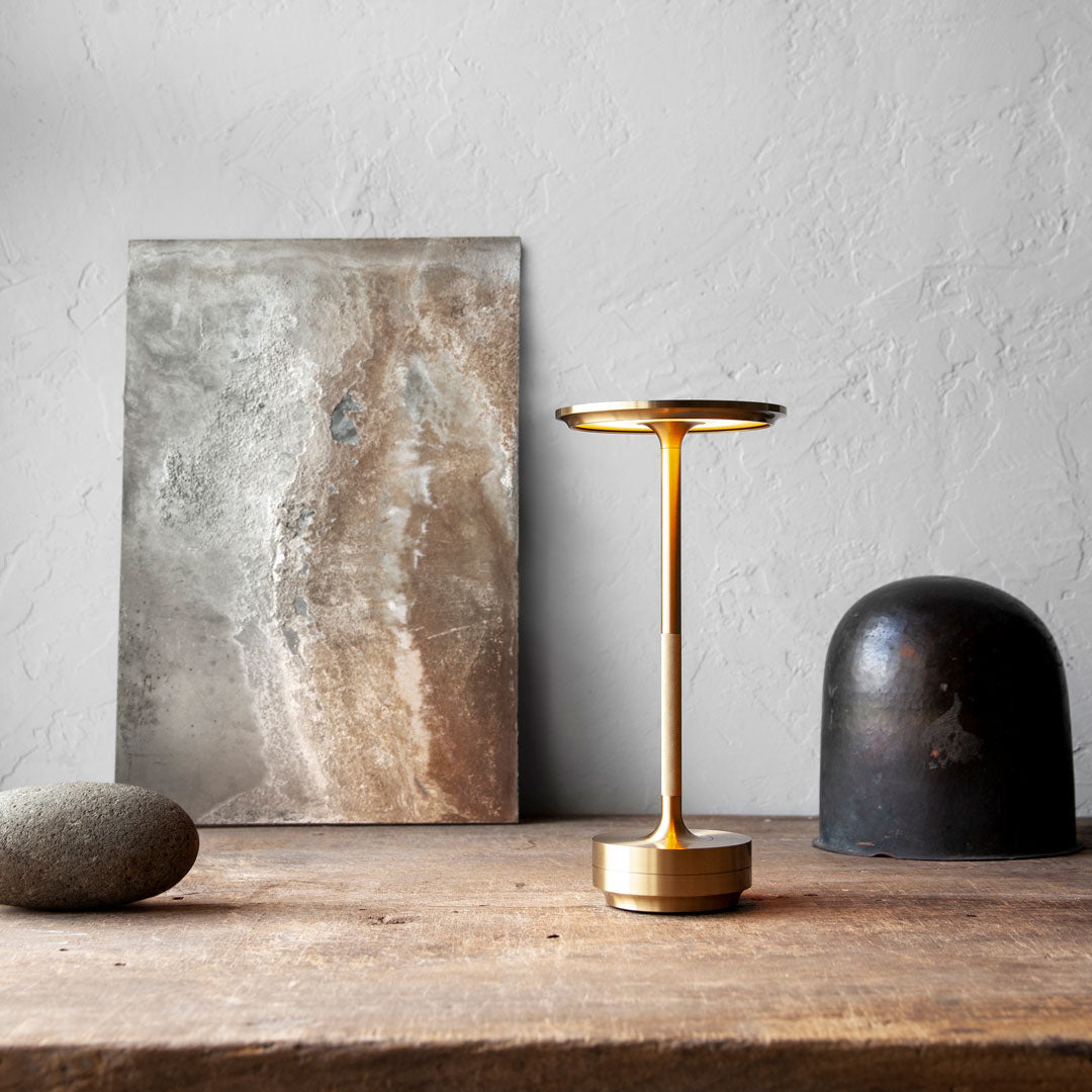 Gold and bronze lamp beside textured gray wall art, featuring earthy tones and natural stone elements.