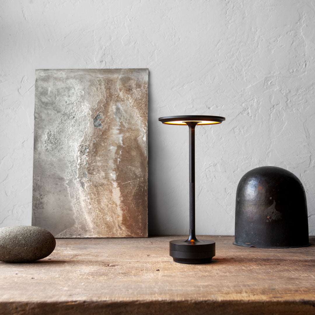 Modern black lamp with warm light, gray stone artwork, and earthy tones on a rustic wooden table. Stylish and minimalistic.