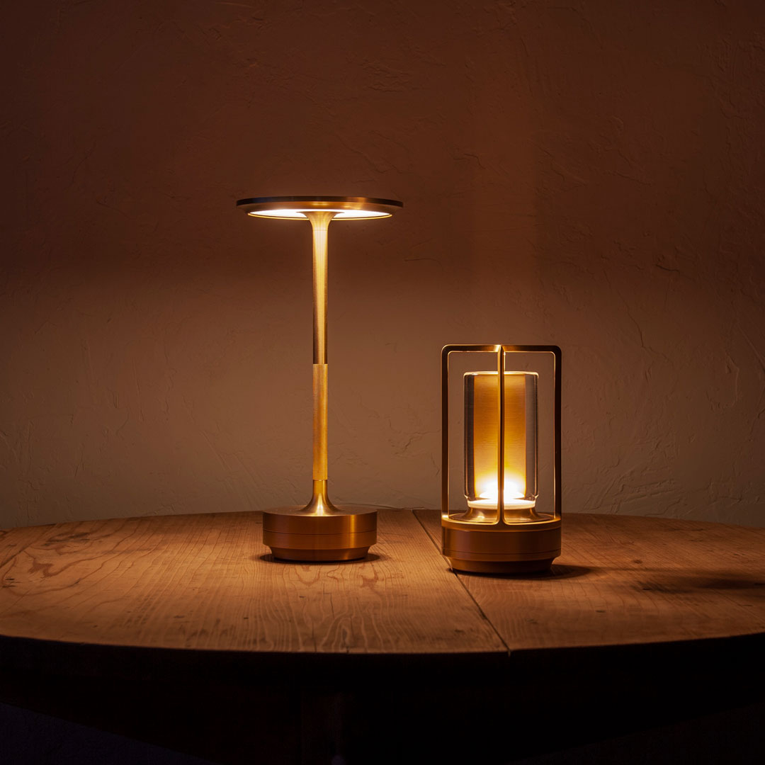 Gold metallic table lamps with warm amber glow, set on a rustic wooden table against a dark wall.