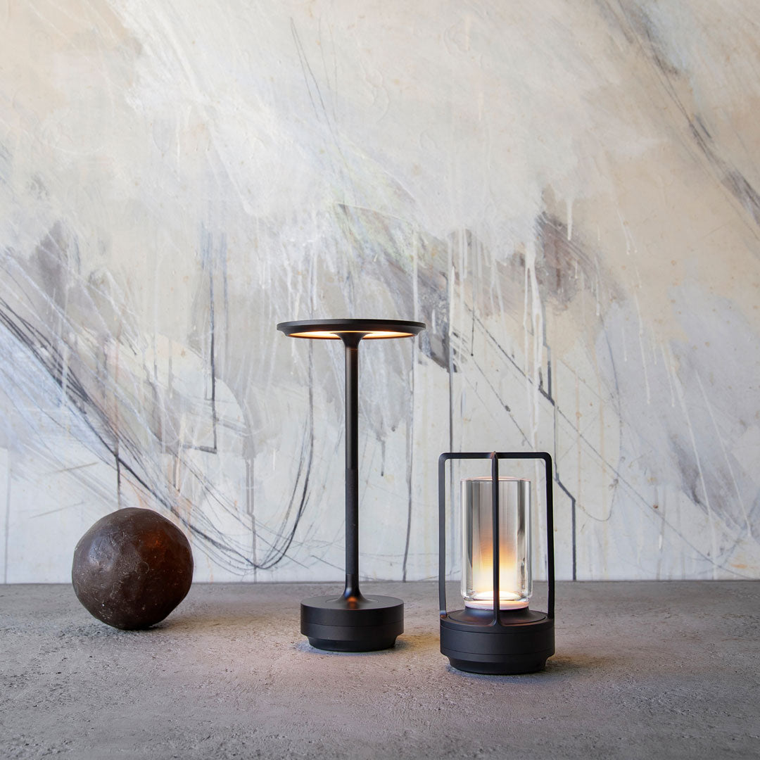 Modern black lamp with warm light, glass lantern, and textured gray background featuring abstract patterns.