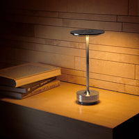 Sleek black lamp with a metallic base on a warm-toned stone countertop, illuminated against textured wall backdrop.