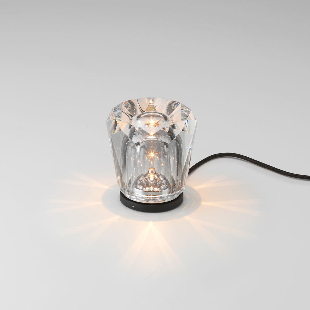 Crystal lamp with a clear, faceted design and soft golden light reflections on a sleek black base.