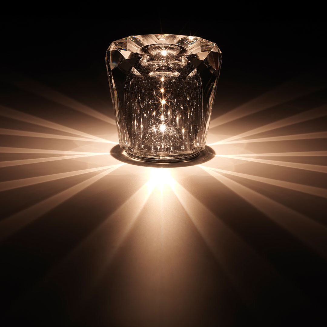 Crystal candle holder casting warm, golden light in a striking starburst pattern on a dark background.