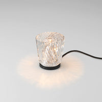 Clear cut crystal lamp with a swirling pattern illuminated by soft, warm light against a sleek black base.