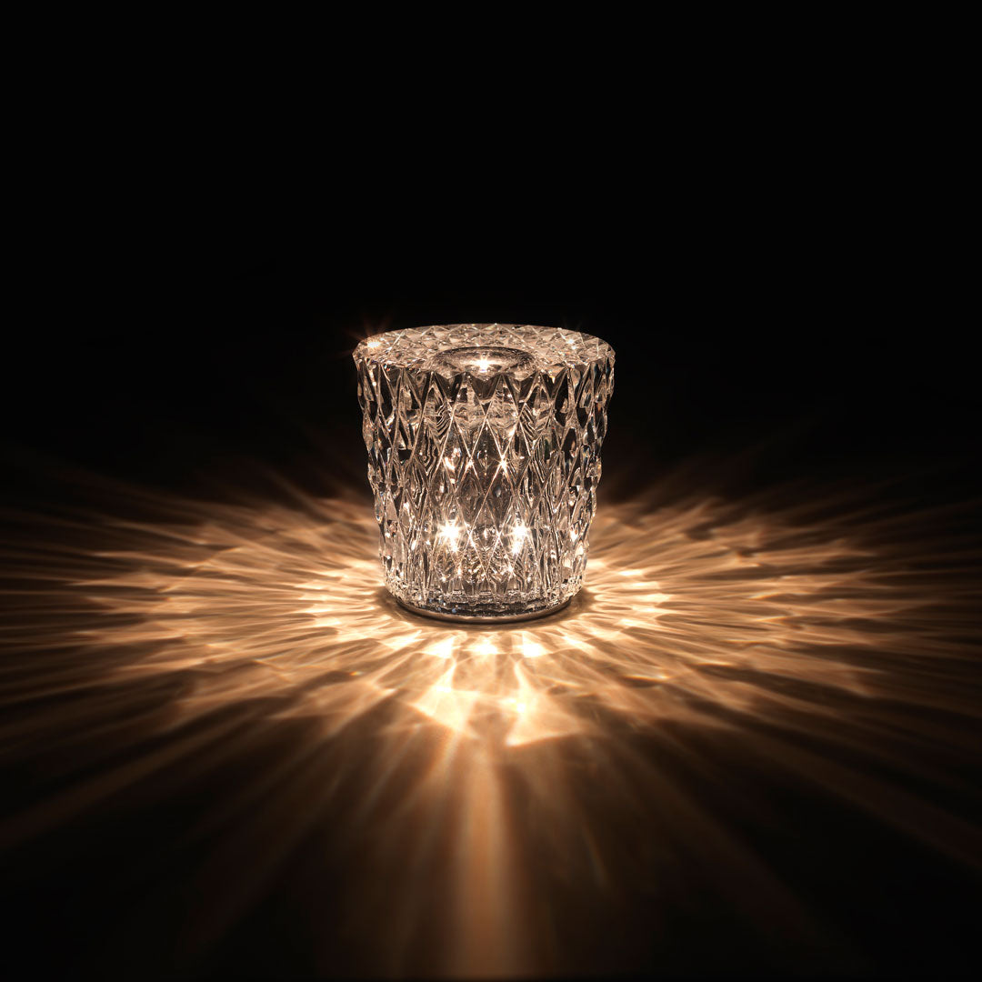 Crystal candle holder casting warm golden light, featuring a diamond cut pattern against a dark background.