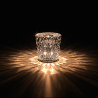 Crystal candle holder casting warm golden light, featuring a diamond cut pattern against a dark background.