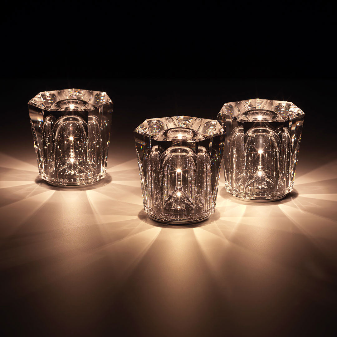 Set of three clear glass candle holders with intricate patterns, reflecting warm golden light. Ideal for elegant decor.