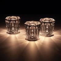 Set of three clear glass candle holders with intricate patterns, reflecting warm golden light. Ideal for elegant decor.