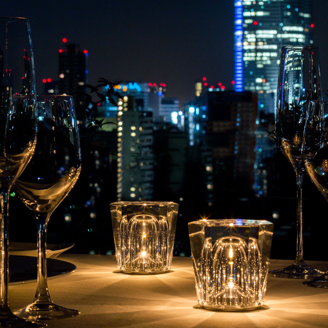Elegant glass candle holders with a sparkling pattern, set against a glowing city skyline at night.
