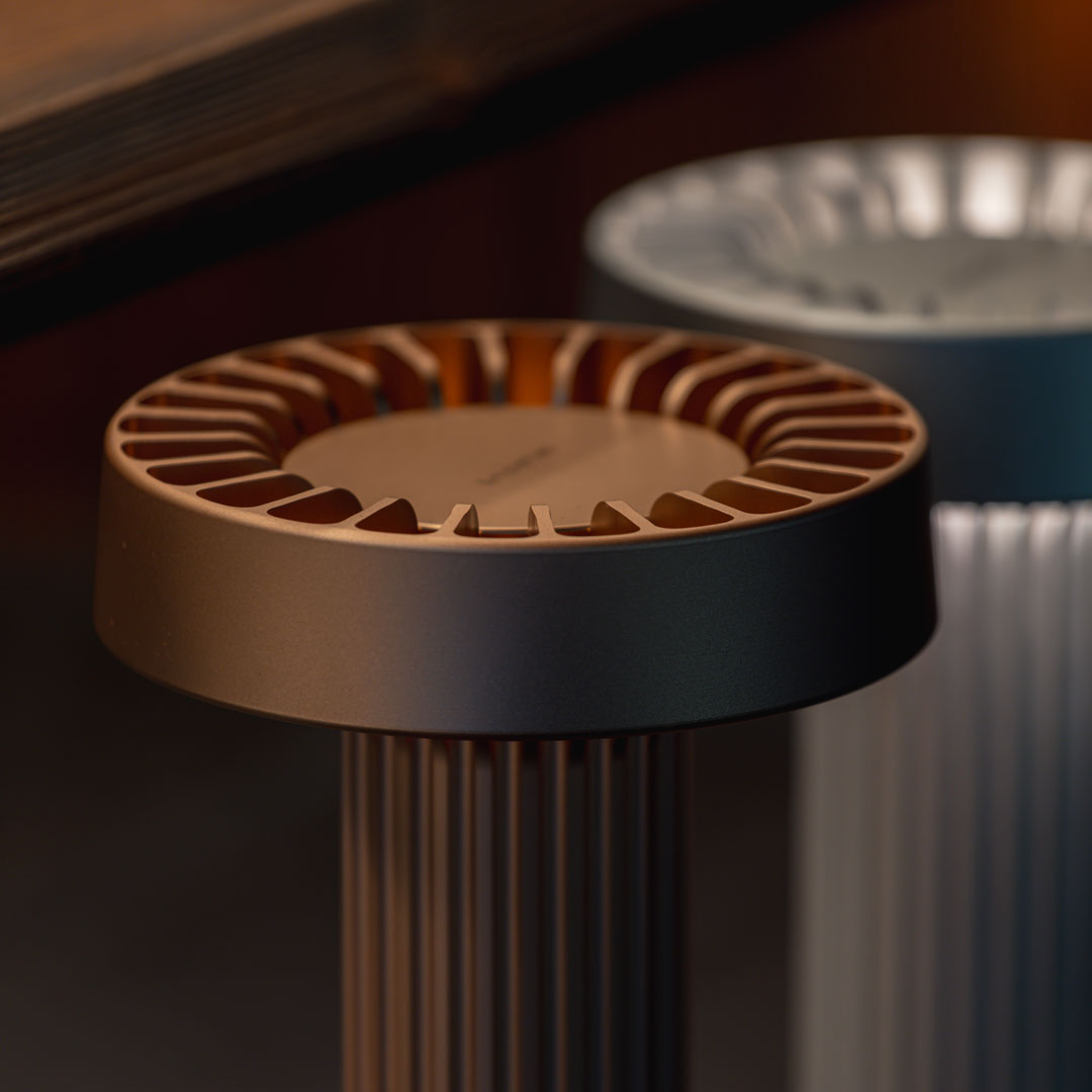 "Close-up of sleek bronze and silver fan bases with textured patterns, set against a dark background."