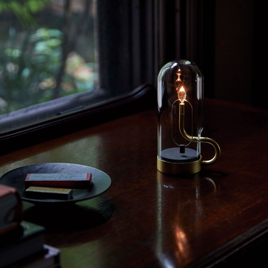 Glass lamp with gold base, clear dome, and black accents on a dark wooden table. Soft lighting enhances the colors.