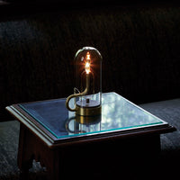 Elegant glass lamp with warm gold accents, set on a reflective glass table against a textured dark background.