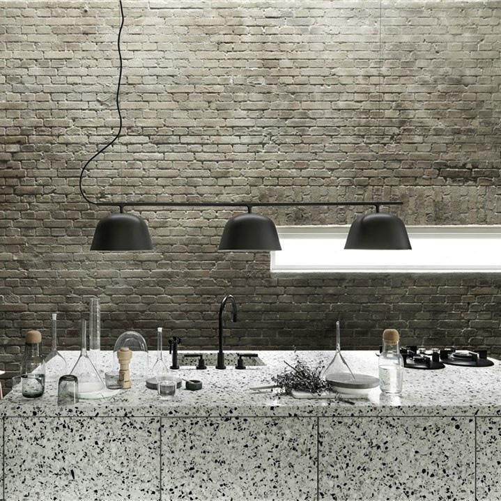 Three black pendant lights hanging above a textured gray and white terrazzo countertop in a minimalist kitchen setting.