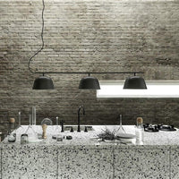 Three black pendant lights hanging above a textured gray and white terrazzo countertop in a minimalist kitchen setting.