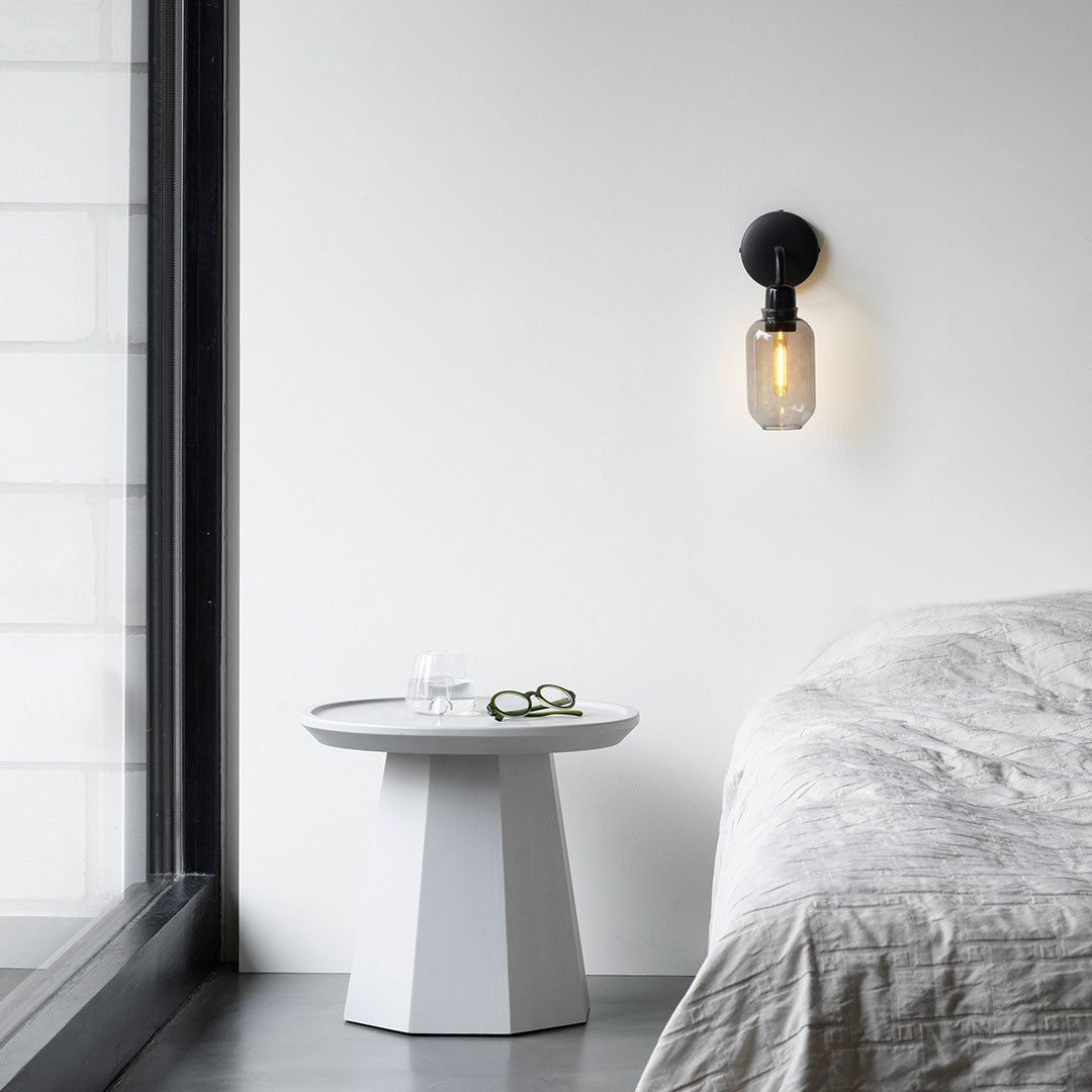 "Modern black wall sconce with clear glass and warm golden light, contrasting against a soft white wall backdrop."