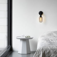 "Modern black wall sconce with clear glass and warm golden light, contrasting against a soft white wall backdrop."