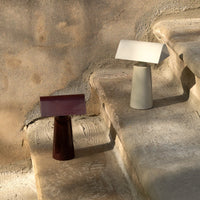 "Two modern lamps in earthy tones: one burgundy and one light gray, set against a textured stone background."