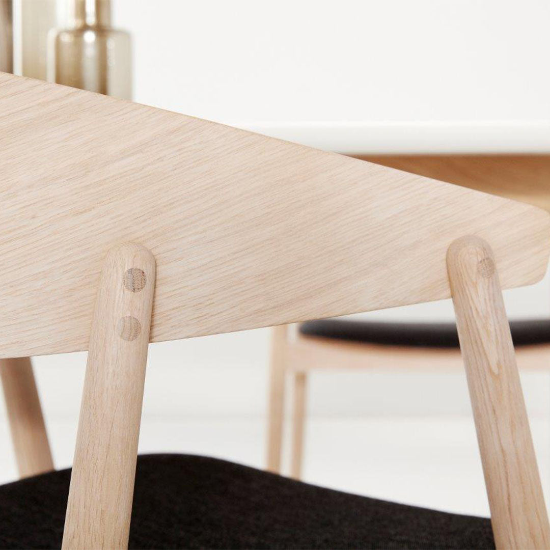 Light wood grain with a smooth finish, contrasted by a black cushioned seat, featuring subtle circular patterns.