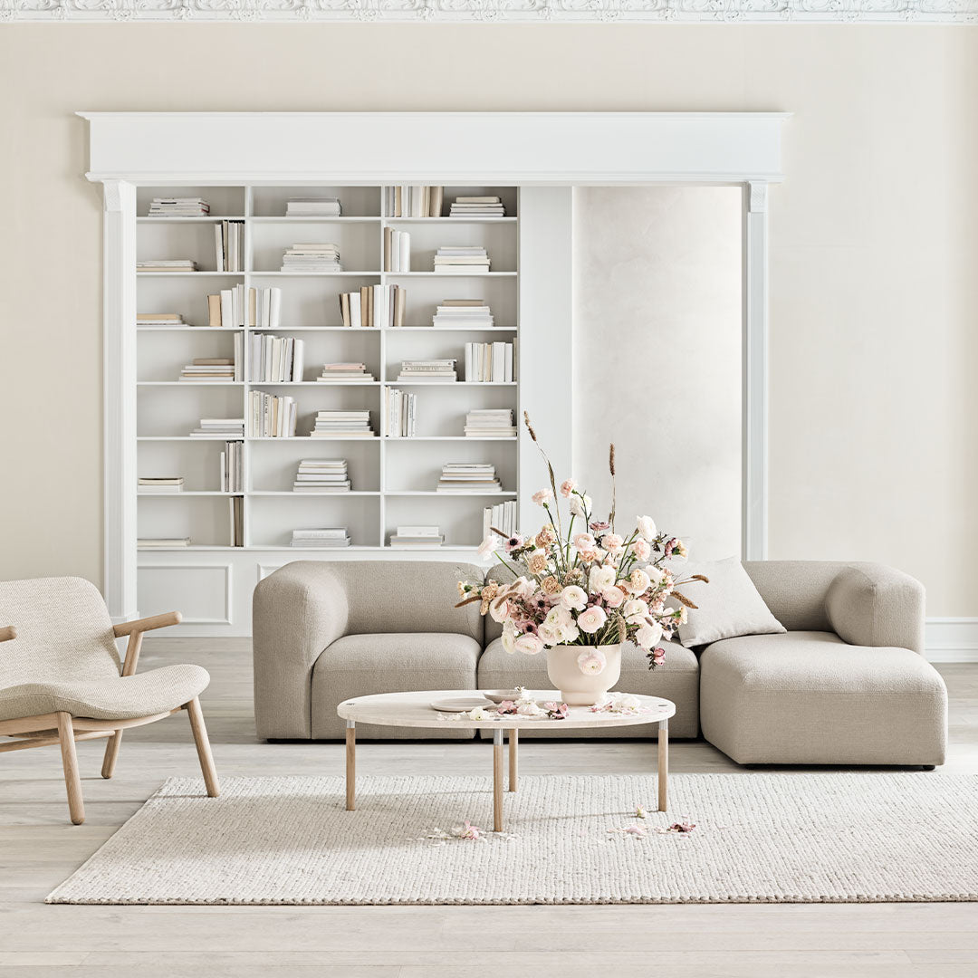 Light beige sofas and armchair with soft white accents, accompanied by a pastel floral arrangement on a neutral rug.