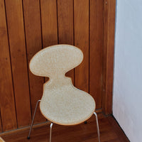 Beige speckled chair with a unique curvy design against a wooden backdrop. Modern and stylish decor accent.