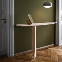 Light wood console table with smooth, minimalist design against olive green wall, highlighting natural textures and tones.