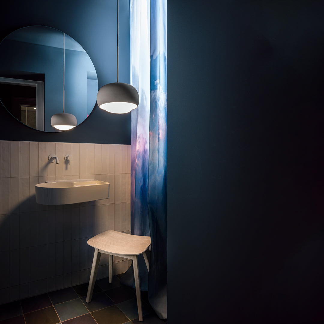 "Dark blue walls, light gray sink, abstract blue and pink patterned curtain, and white stool create a modern bathroom aesthetic."