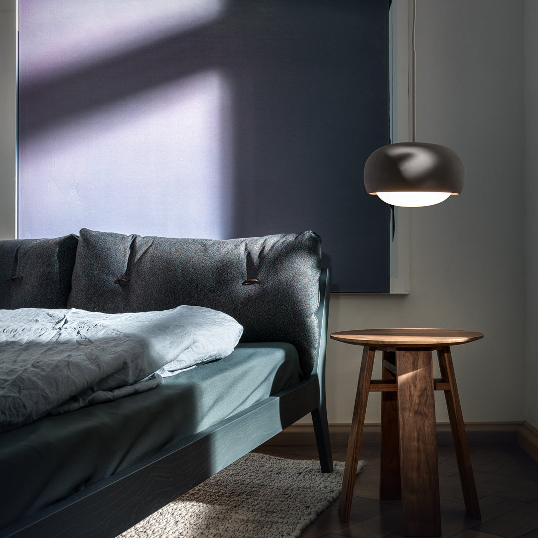 Cozy bedding in shades of gray, complemented by a dark wood table and a sleek black lamp against a muted purple backdrop.
