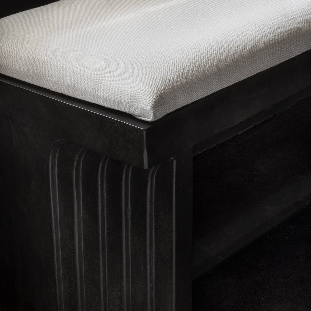 Black bench with textured sides and a soft white cushion, featuring elegant, modern design elements.